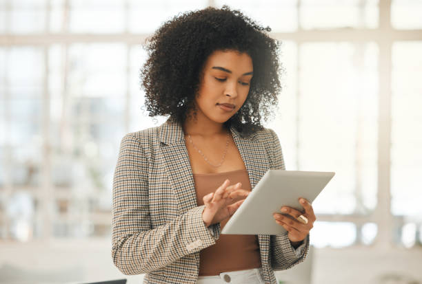 Young businesswoman using a digital tablet. Focused designer standing in her agency. Creative entrepreneur working on a wireless device. Young architect using an online app on her wireless tablet.