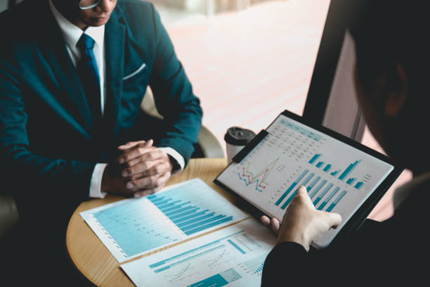 Two business partnership coworkers analysis strategy and gesturing with discussing a financial planning graph and company budget during a budget meeting in office room.