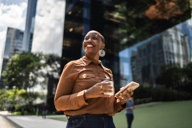 Business woman holding smartphone and contemplating outdoors