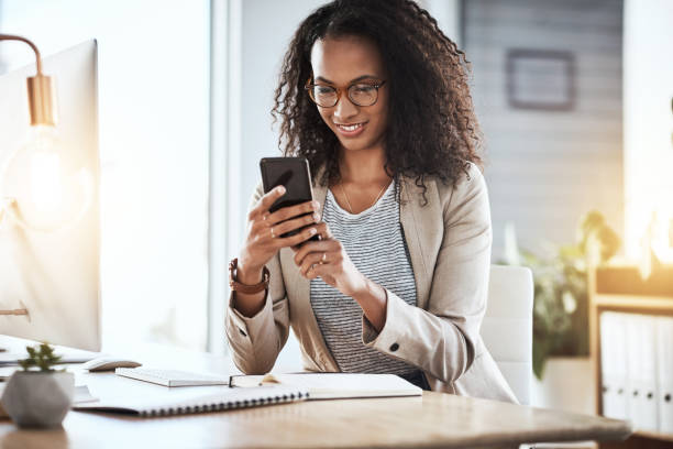 Shot of a businesswoman using her cellphone while sitting at her desk